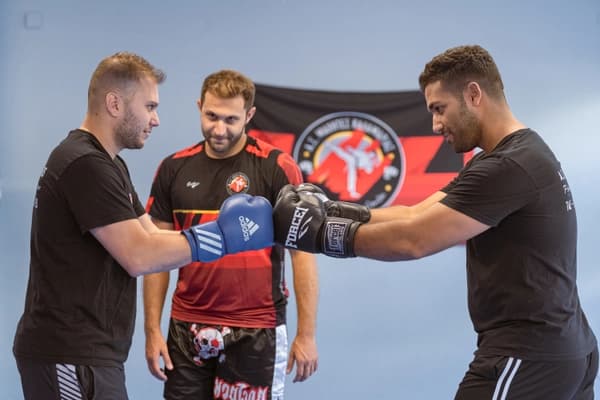 Οι δύο αθλητές ενώνουν τις γροθιές τους και απο πίσω ο προπονητής τους παρακολουθεί.