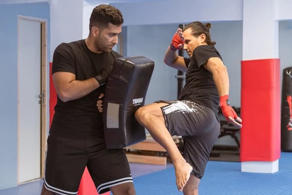 O προπονητής κρατάει προστατευτικό και ο αθλητης κλωτσάει με το γόνατο του το προστατευτικό.