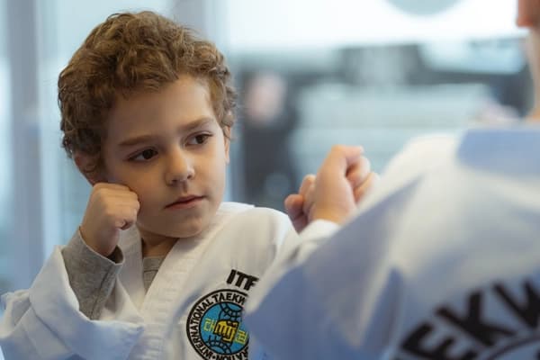 Ενα σγουρομάλλικο παιδί με την στολή του συλλόγου κάθεται σε θέση προστασίας με τα χέρια του ψηλά πάνω και κάνοντας τα γροθιές.